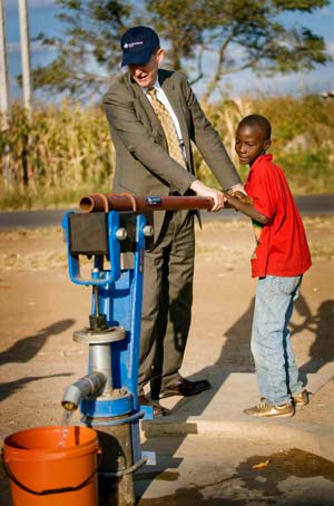 Photo of Australian Ambassador John Courtney helping a young boy pump water from a bore in Zimbabwe